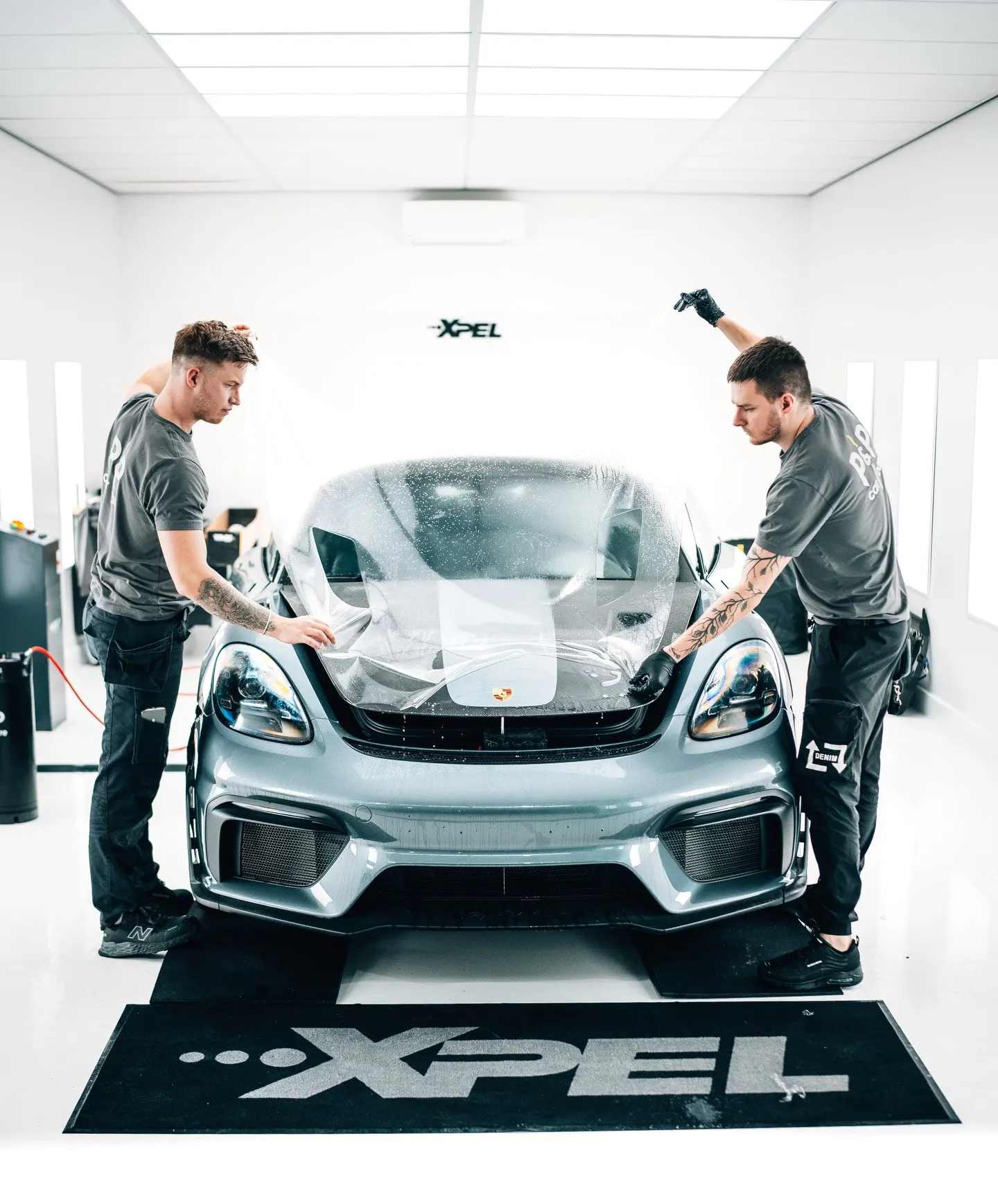 Twee specialisten van P&P Car Care brengen XPEL Paint Protection Film aan op de motorkap van de Porsche 718 Spyder RS