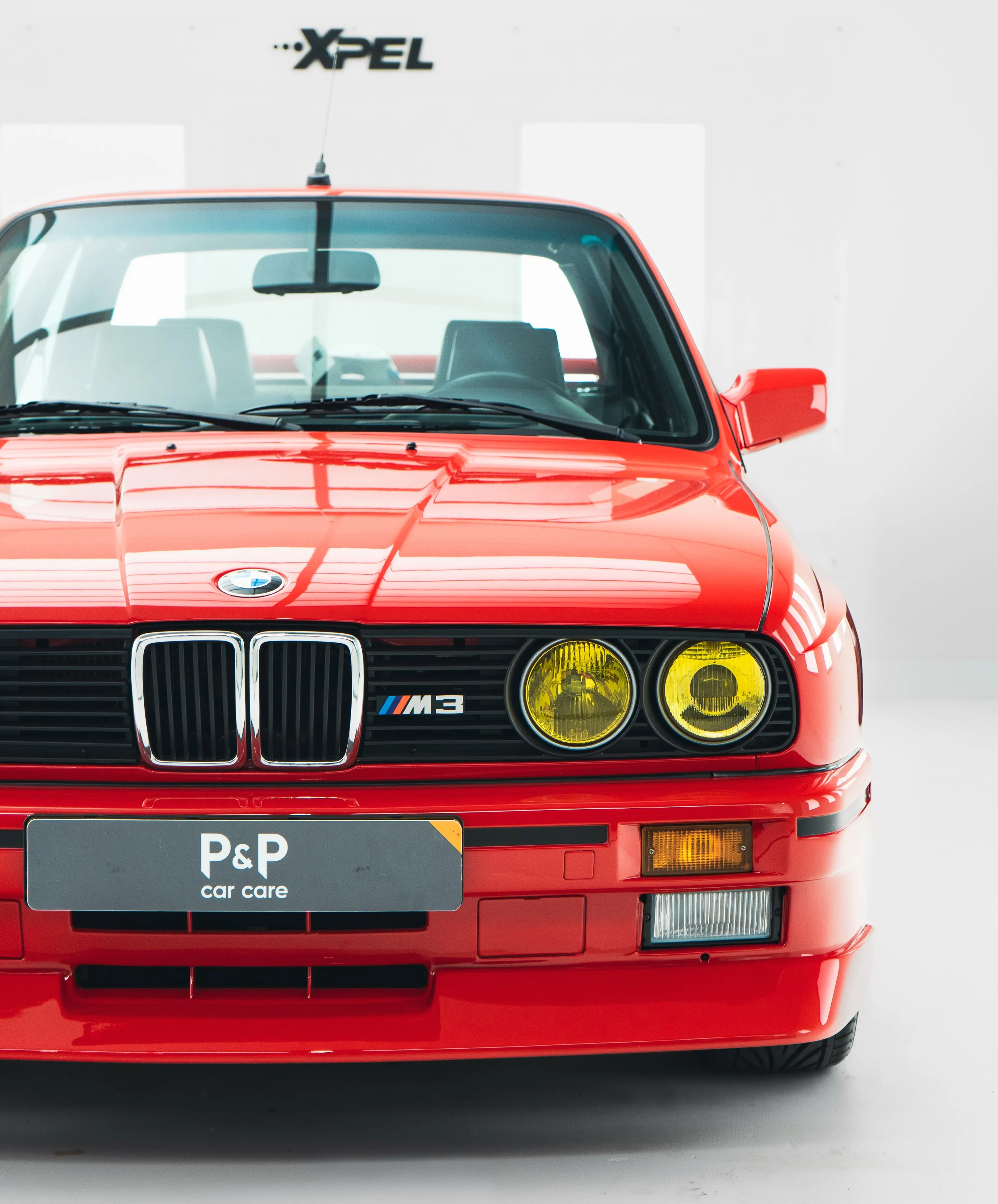 Vooraanzicht van de rode BMW E30 M3 met gele koplampen