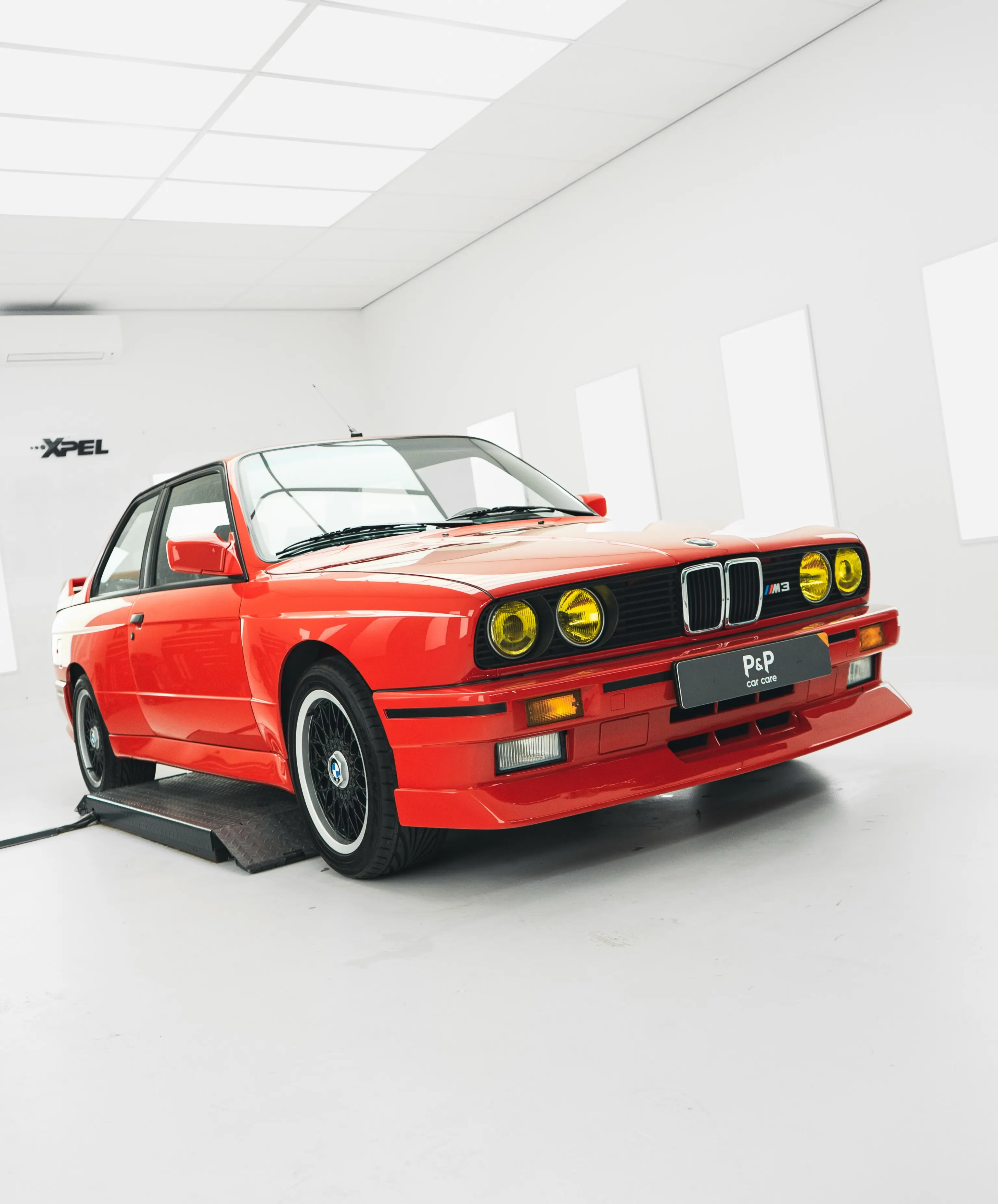 Rode BMW E30 M3 in de studio van P&P Car Care, driekwart vooraanzicht