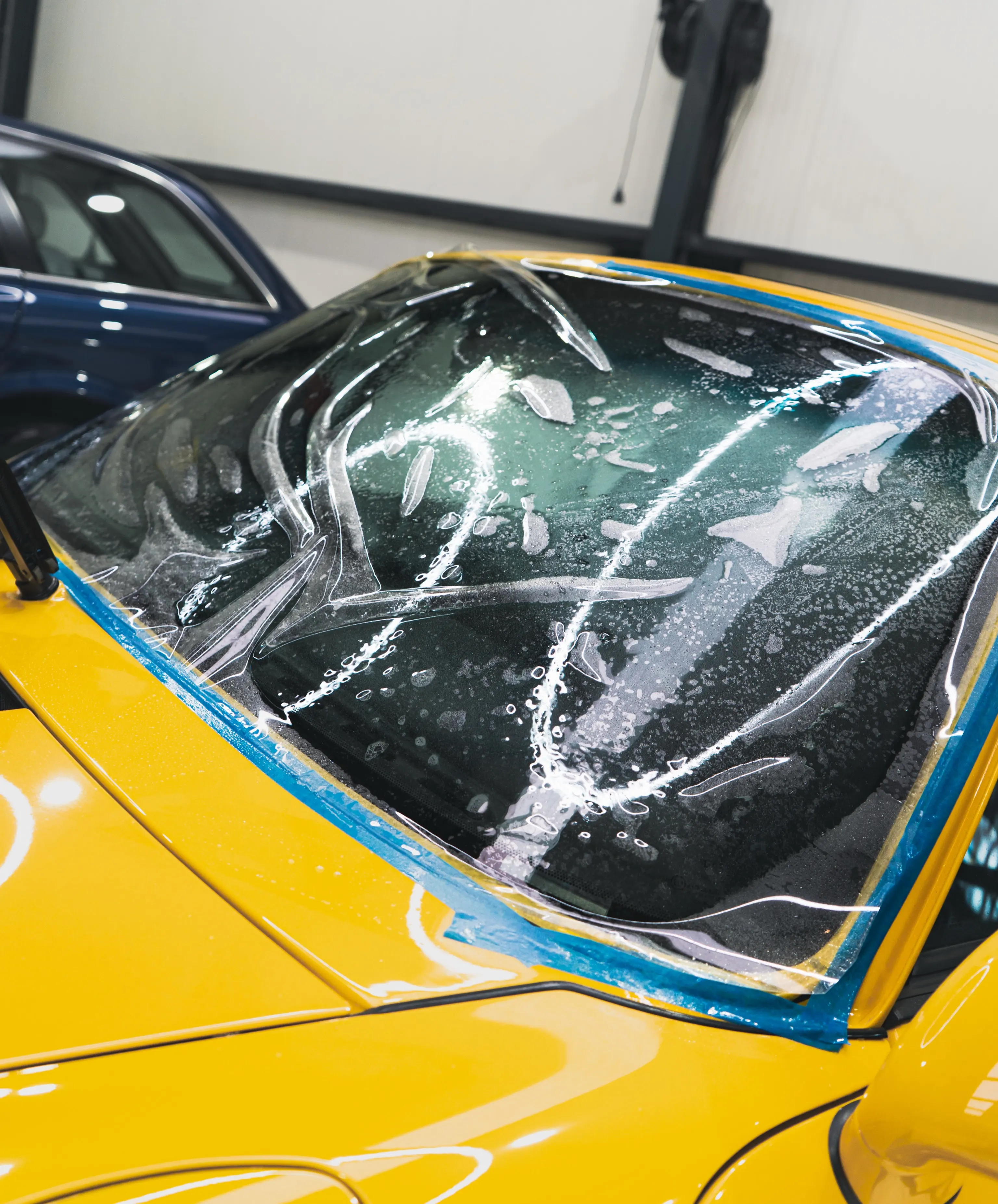 Transparante beschermfolie wordt op de voorruit van de Porsche 993 Turbo aangebracht, afgeplakt met blauw tape