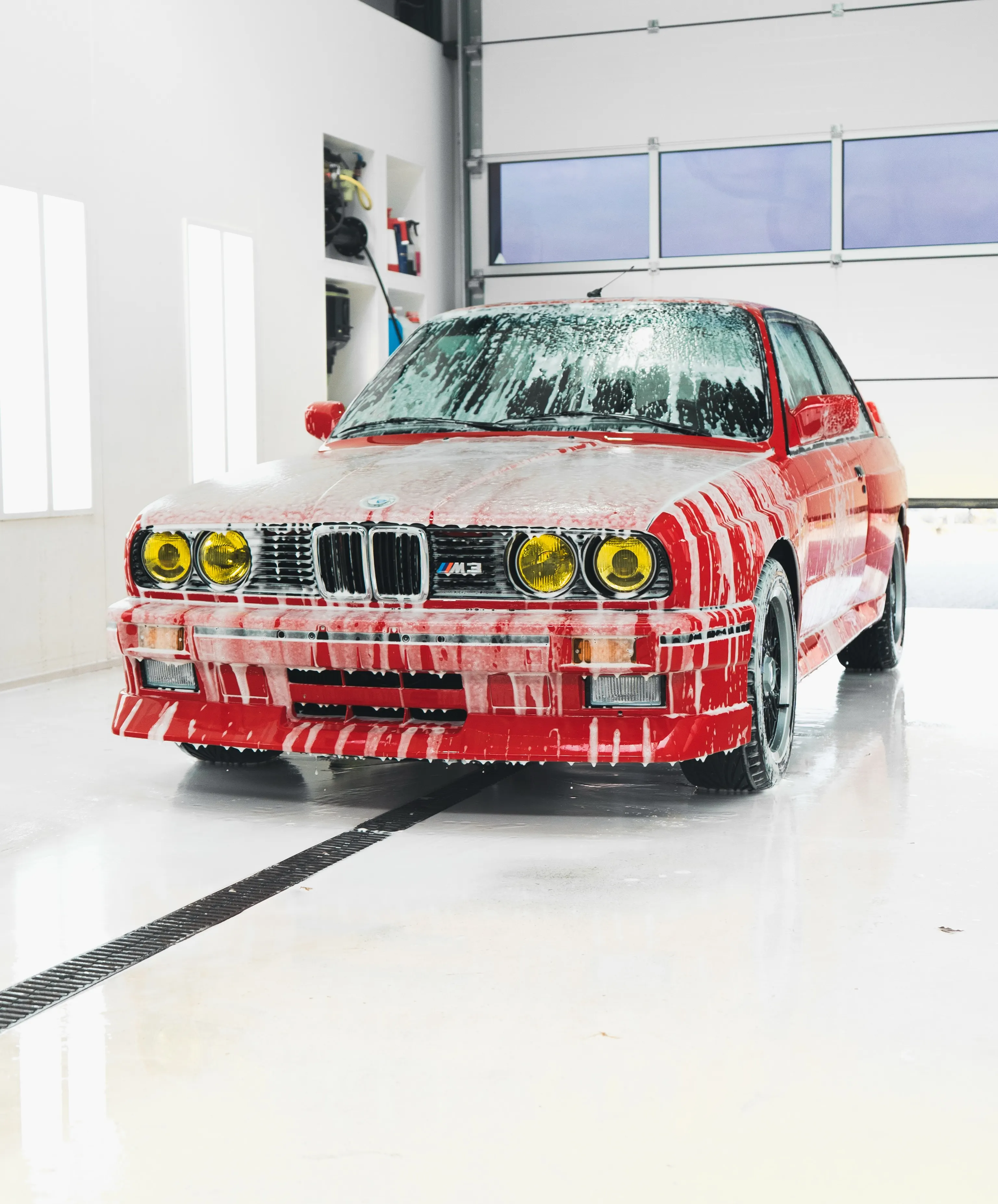 De BMW E30 M3 onder een laag snow foam in de wasbox