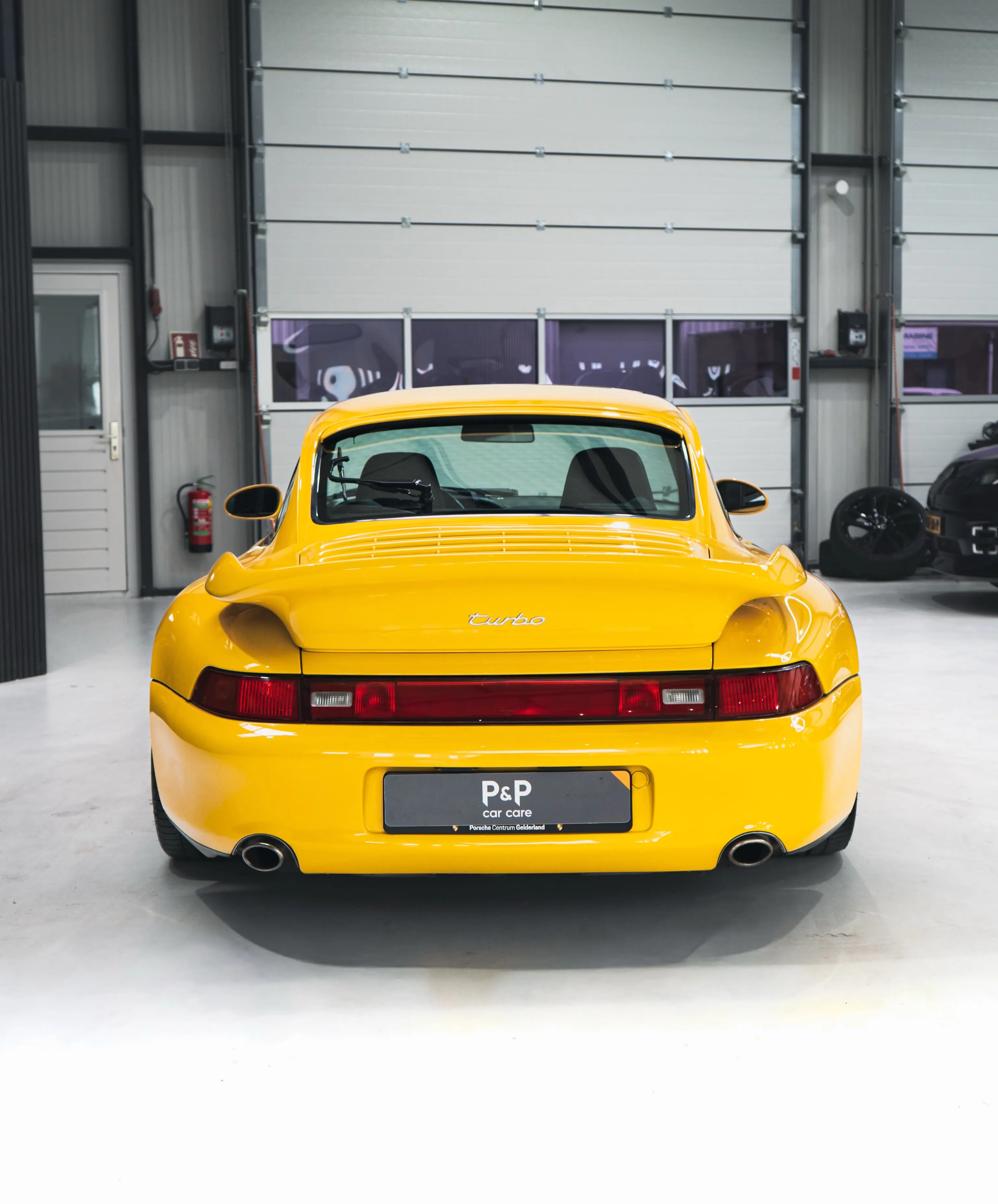 Recht achteraanzicht van de gele Porsche 993 Turbo in de werkplaats
