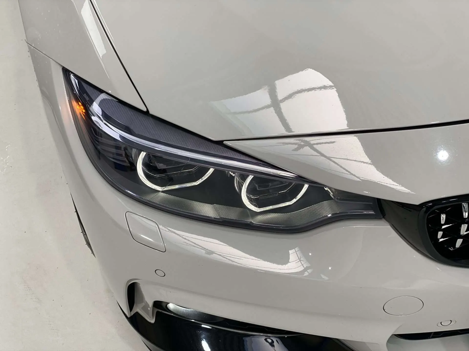 Getinte koplamp van een witte BMW 4 Serie, met de donkere lens tegen de lichte lak