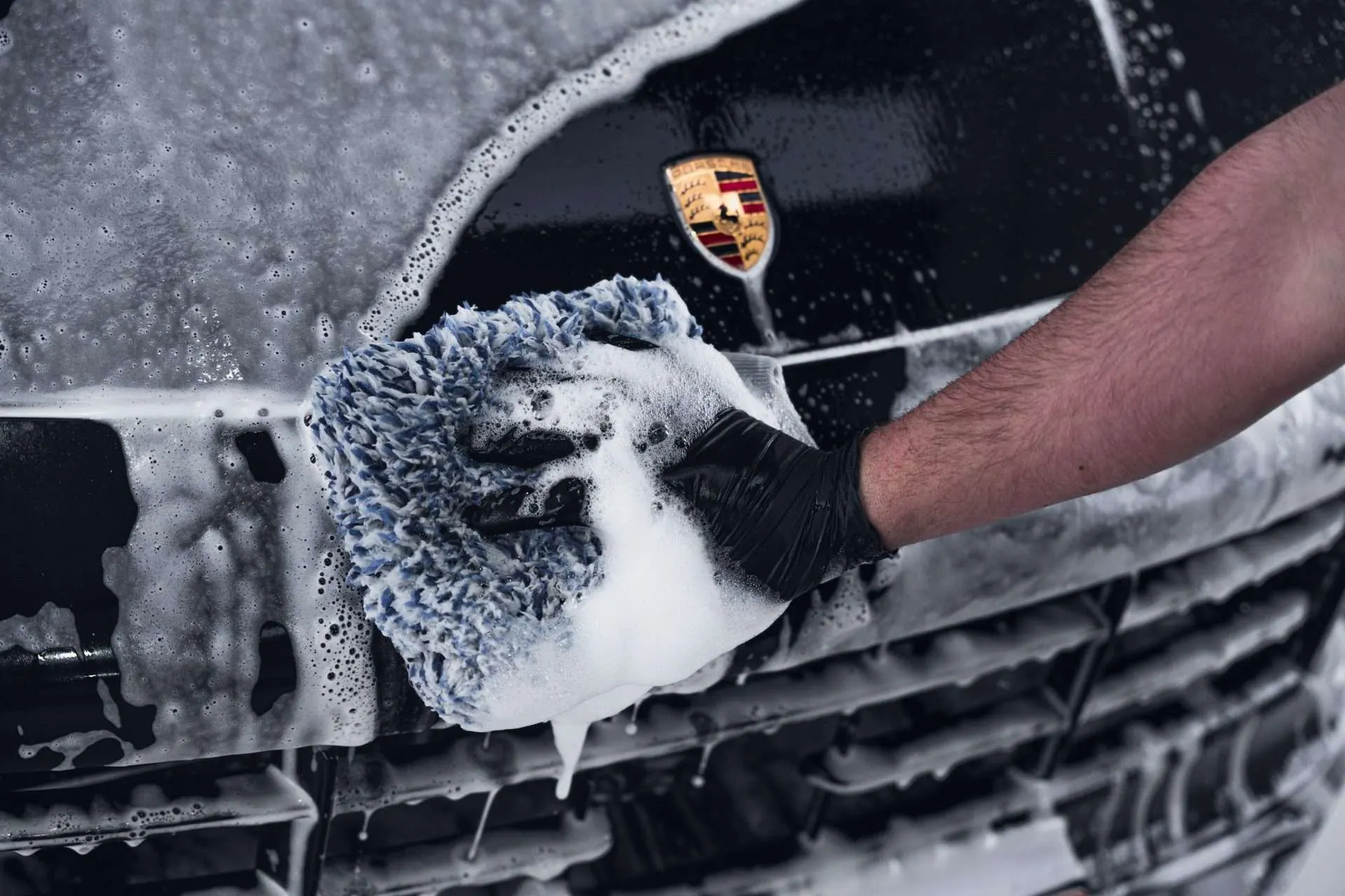 Handwas met een microvezel washandschoen en dik schuim op de neus van een zwarte Porsche