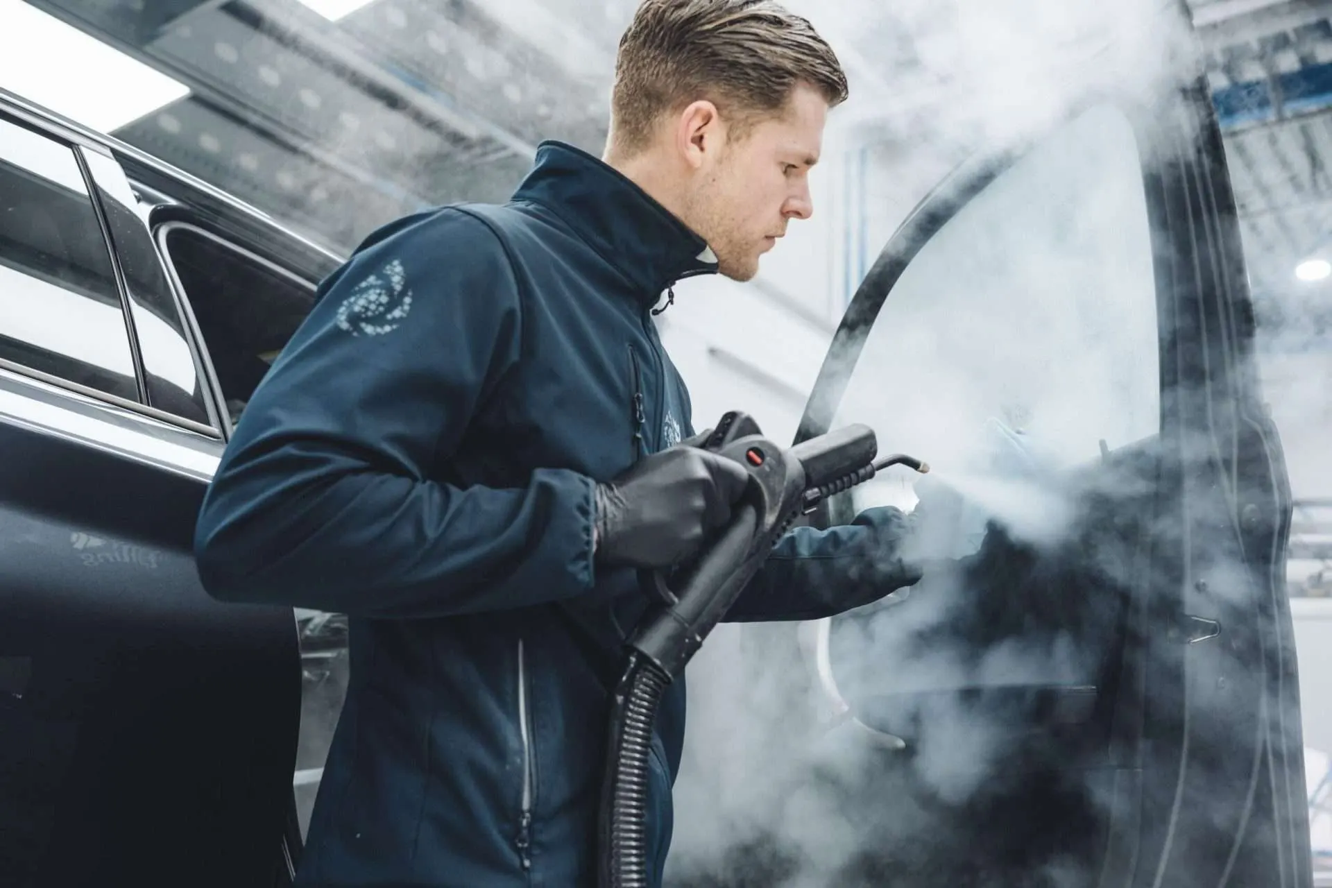 Technicus stoomreinigt het deurframe van een donkere auto