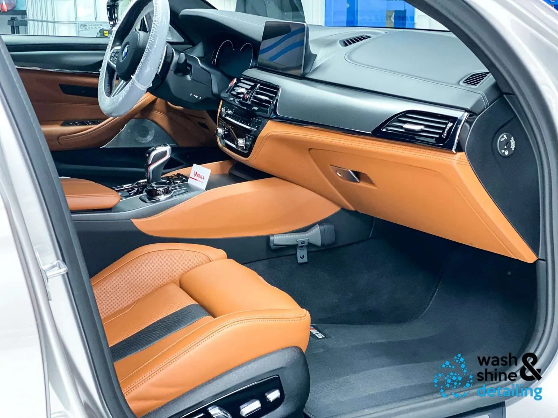 Smetteloos cognac met zwart lederen interieur van een BMW M5, gezien door de geopende bestuurdersdeur