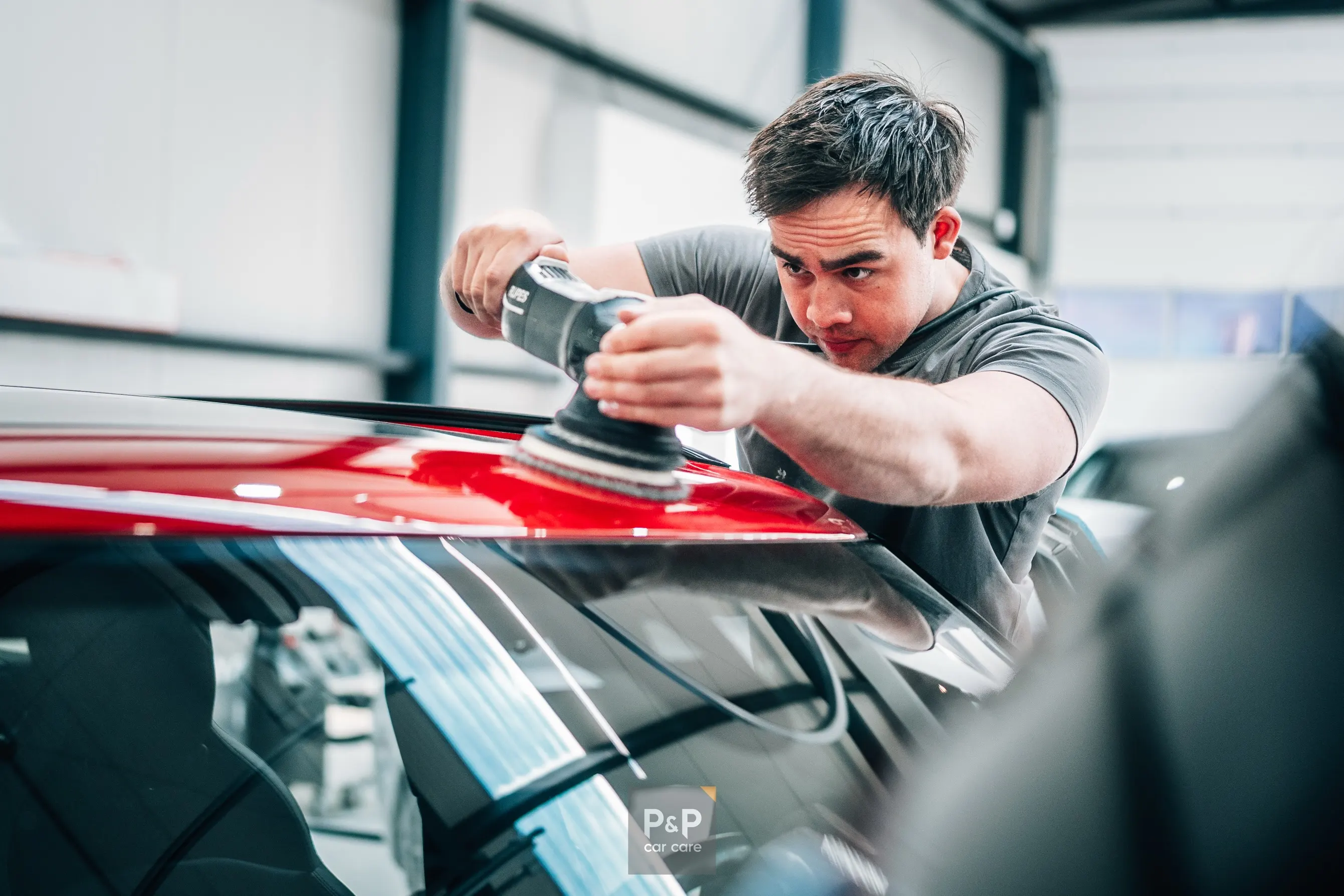 Een specialist van P&P Car Care polijst machinaal het lakwerk van een rode auto