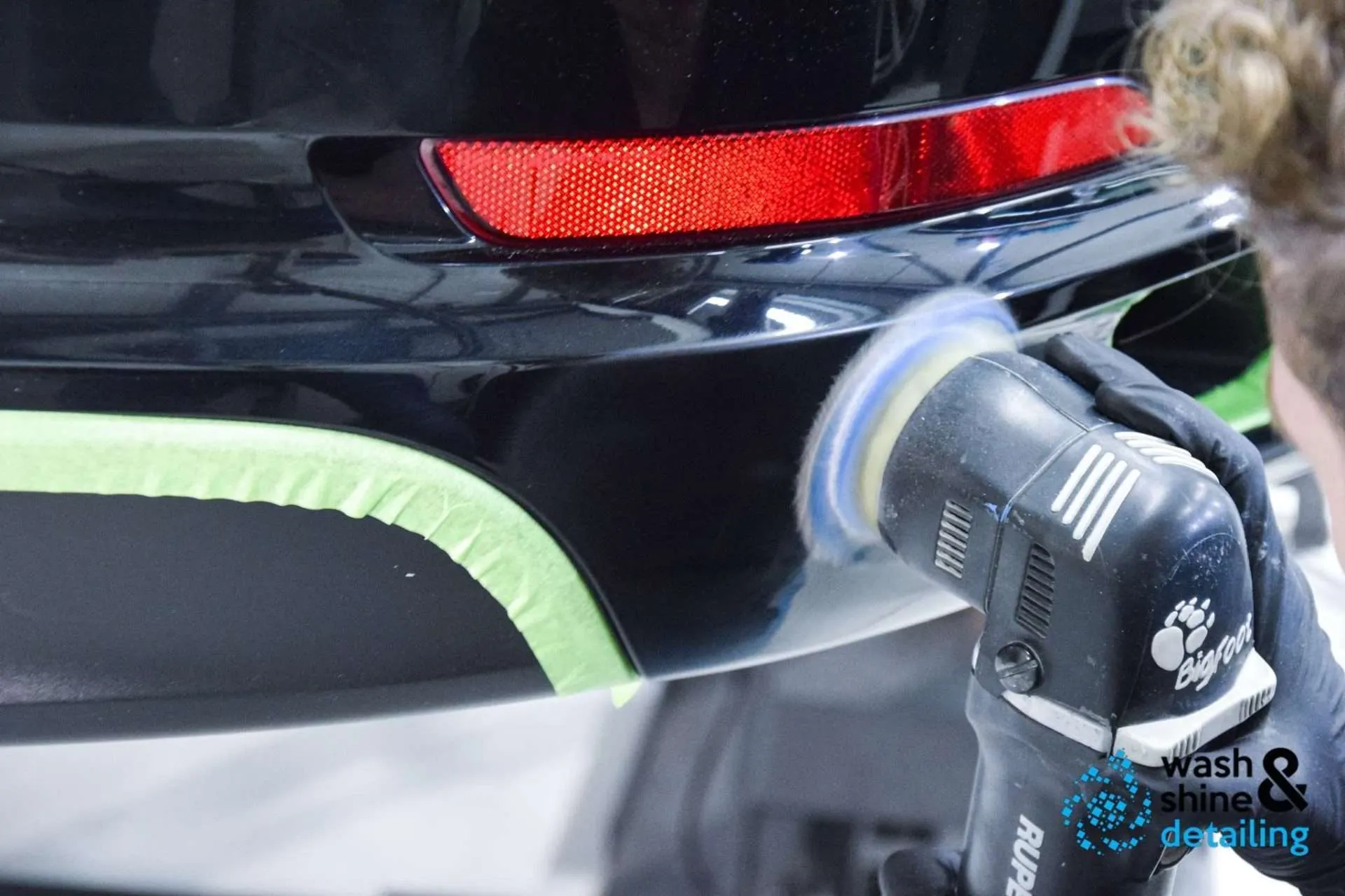 Technicus polijst met een dual-action machine de achterbumper van een zwarte auto
