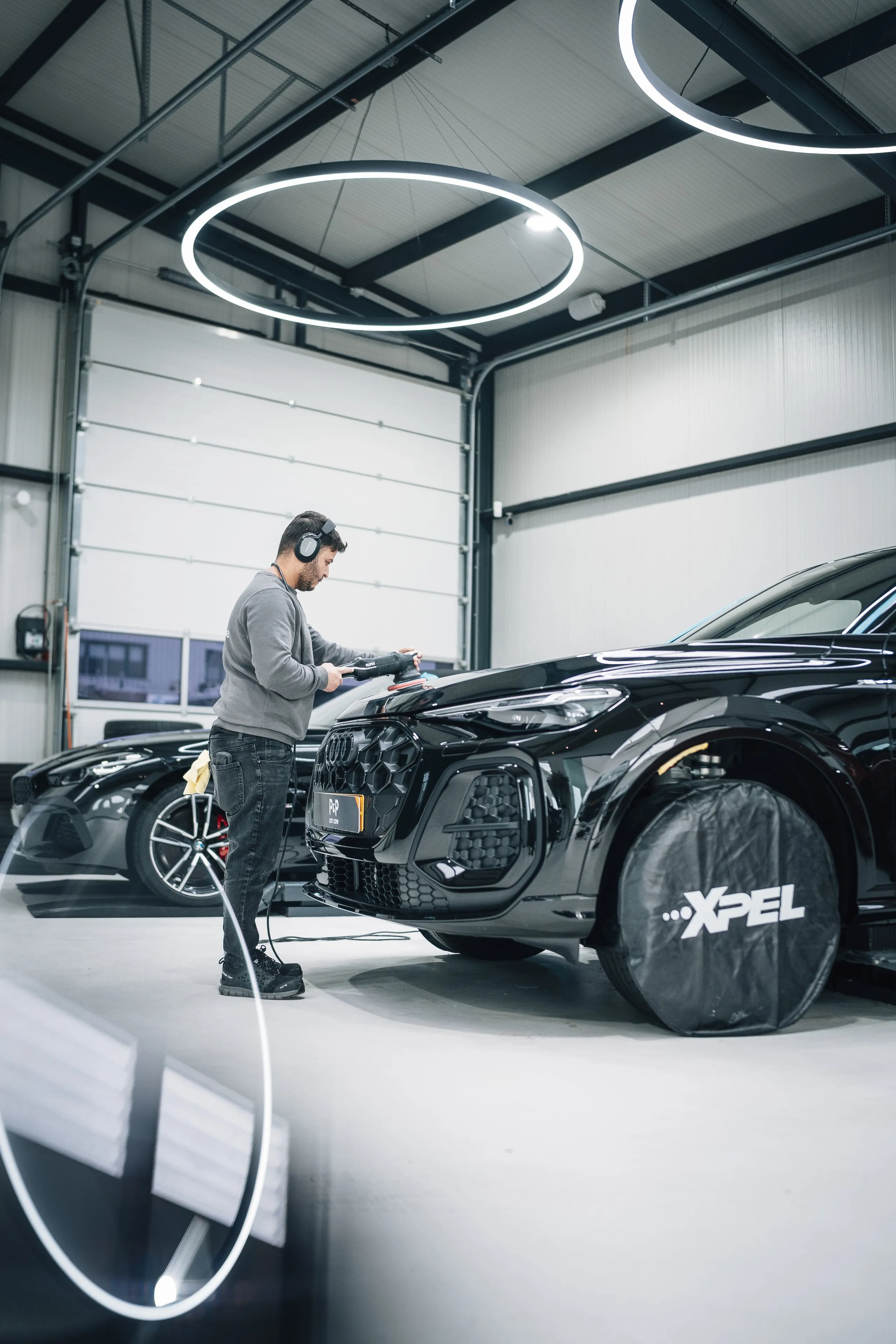 Technicus met gehoorbescherming polijst machinaal de motorkap van een Audi