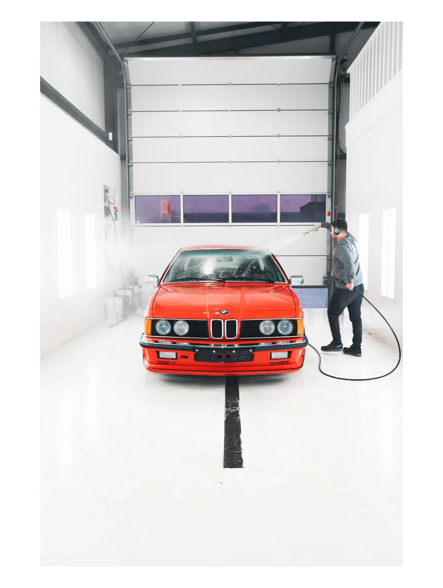 Technicus spoelt een rode BMW 635 CSi af met een hogedrukreiniger in de wasruimte van P&P Car Care
