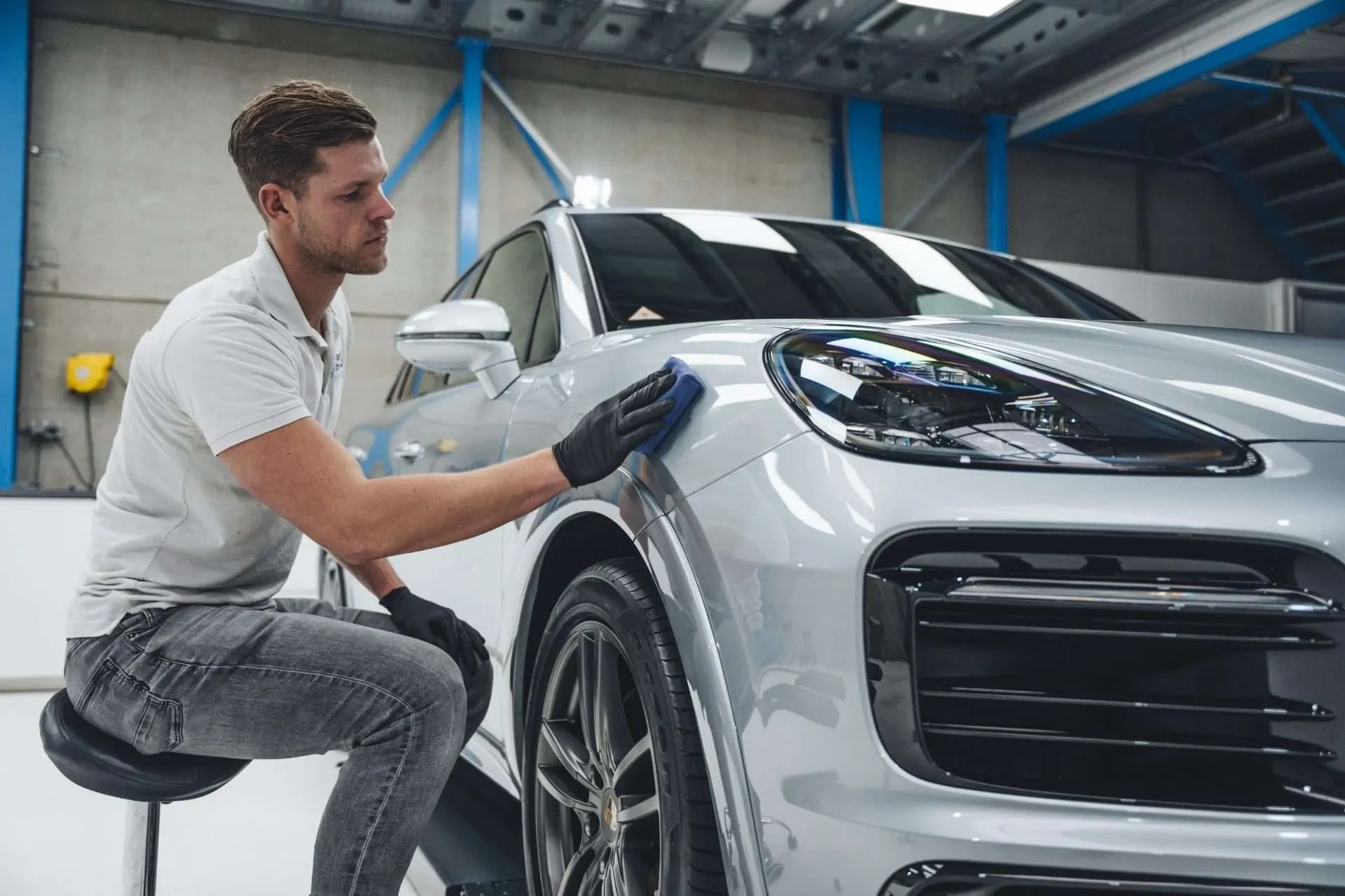 Technicus brengt met een microvezel applicator een coating aan op het voorspatbord van een witte Porsche Cayenne