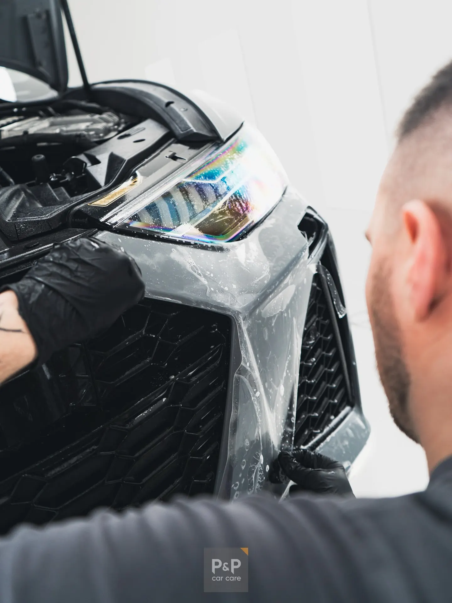 Technicus brengt met een rakel natte Paint Protection Film aan op de voorbumper van een auto